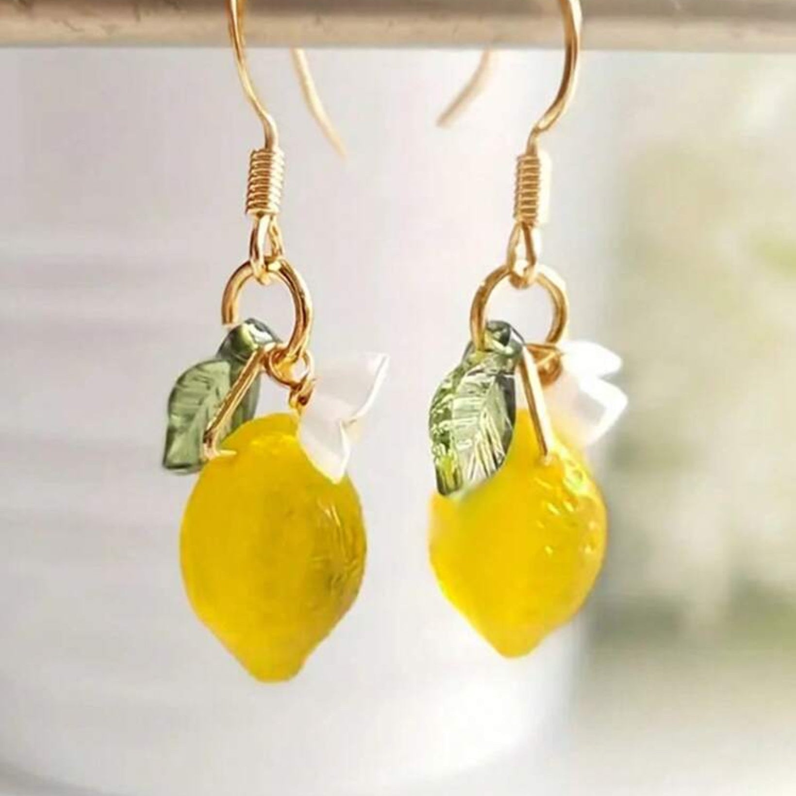 Lemon-shaped earrings with gold hooks and green leaves on a white background