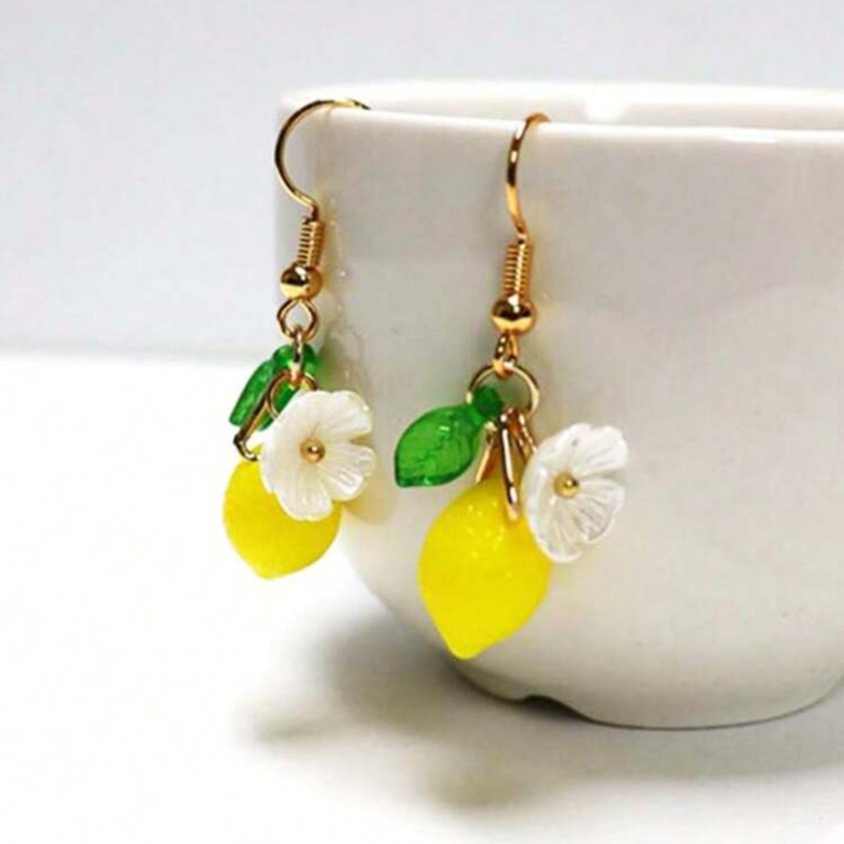 Lemon-shaped earrings with flowers and leaves hanging on a white cup.