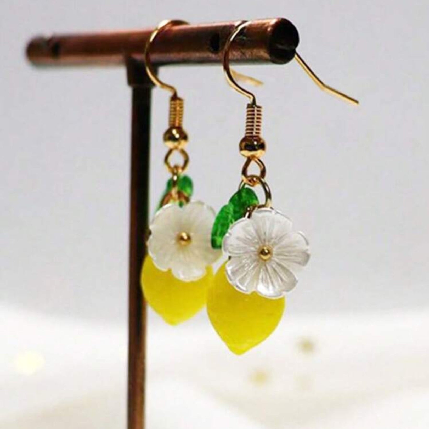 Pair of earrings with yellow leaves and white flowers on a stand against a light background