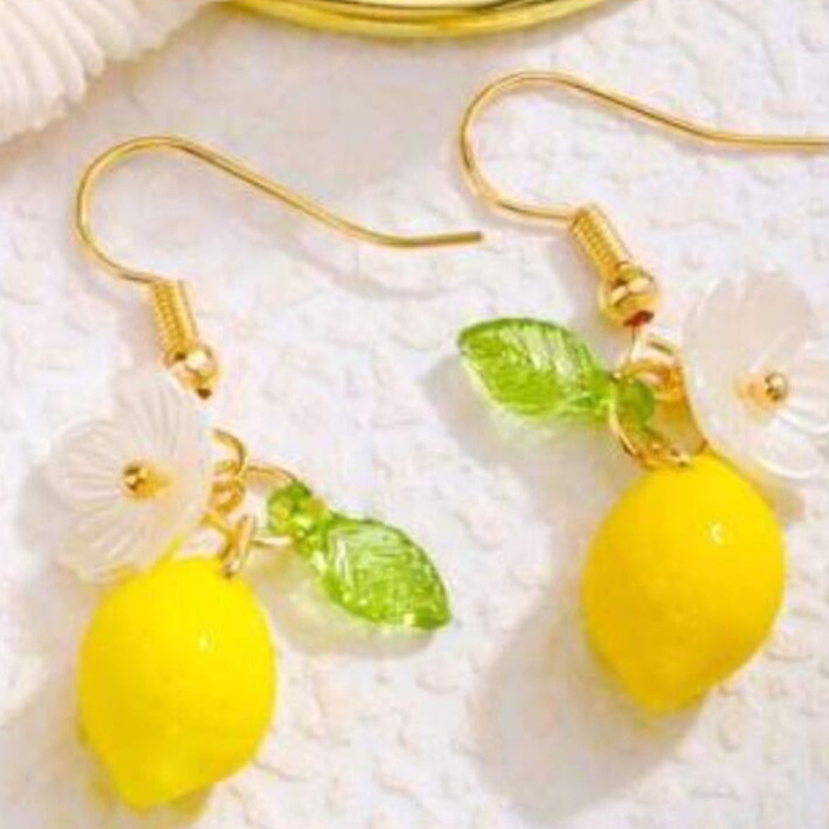 Lemon-shaped earrings with gold hooks on a textured white surface