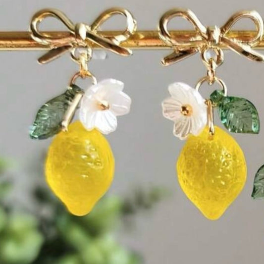 Pair of earrings with lemon and flower charms on a blurred green background