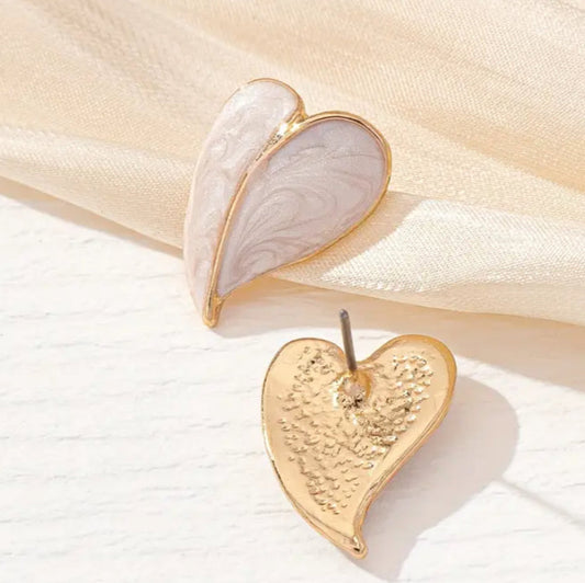 A pair of gold-tone heart earrings with a raised, sculpted center and a polished gold line, displayed on a beige fabric surface.