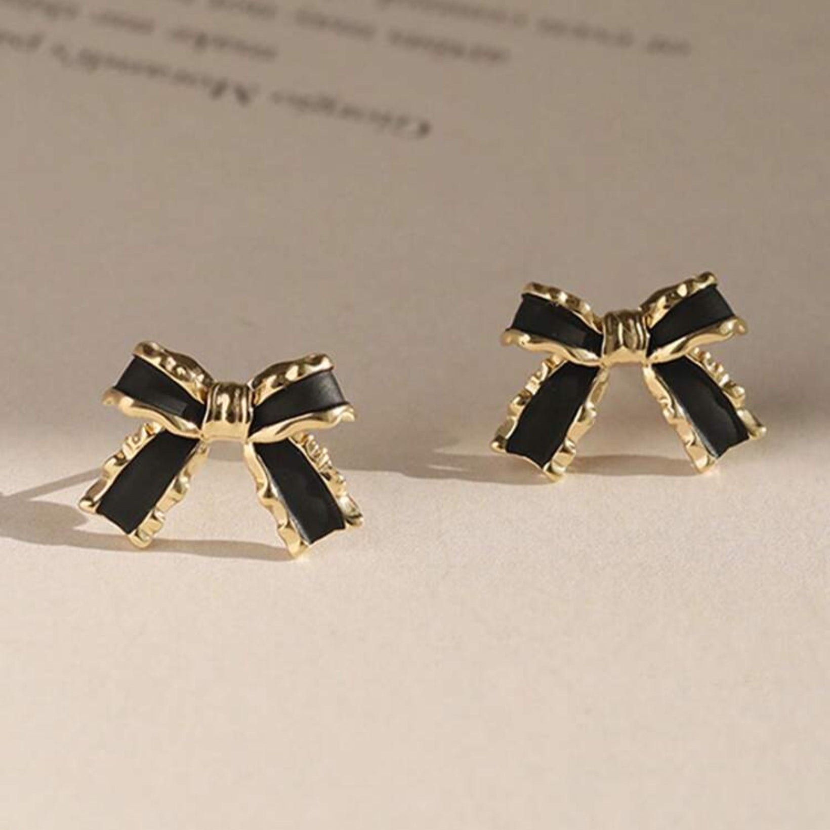 Black & Gold Bow Earrings with black centers and gold outlines on a beige surface.