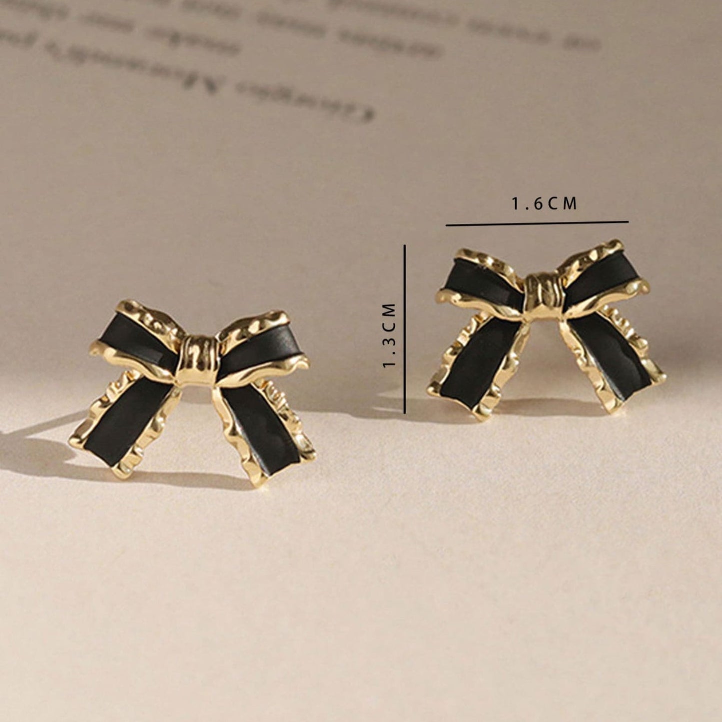 Black & Gold Bow Earrings with gold accents on a beige background