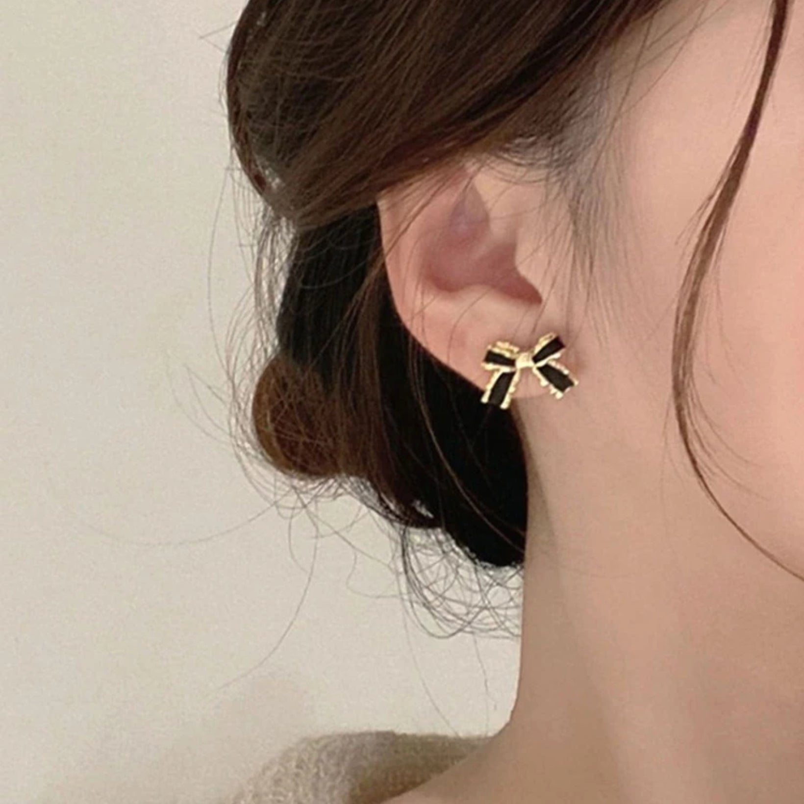 Black and Gold Bow Earrings worn by a person with a neutral background