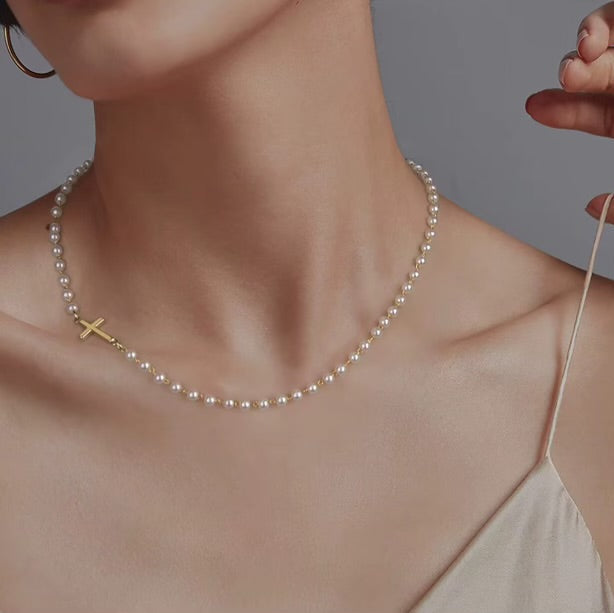 Gold Cross Pearl Necklace with a cross pendant being adjusted on a person against a neutral background
