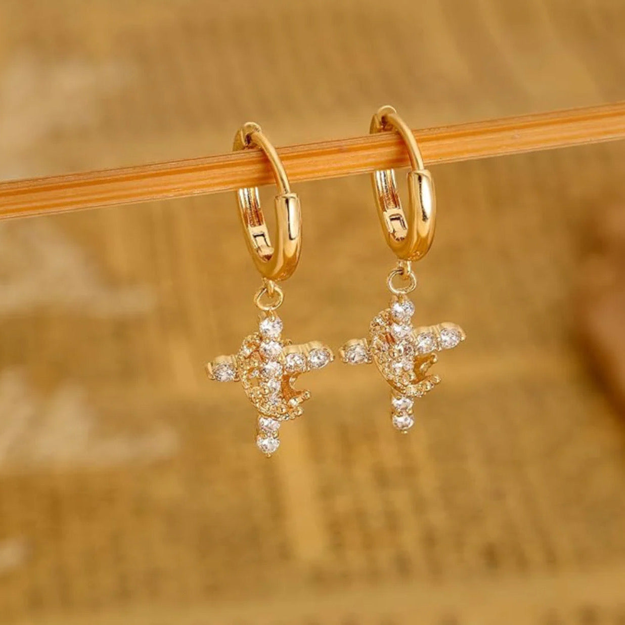 Gold Cross Crown earrings with cubic zirconia stones on a wooden stick against a blurred background