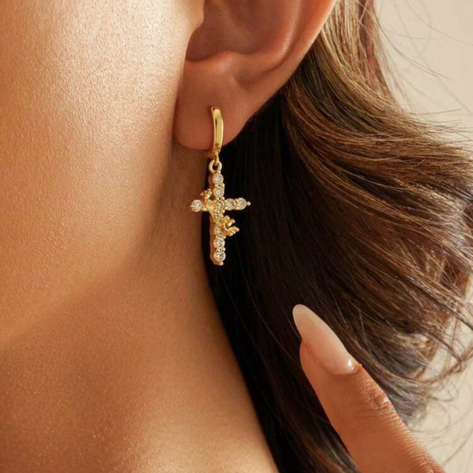 Gold Cross Crown earrings with cubic zirconia stones worn by a person with a blurred background