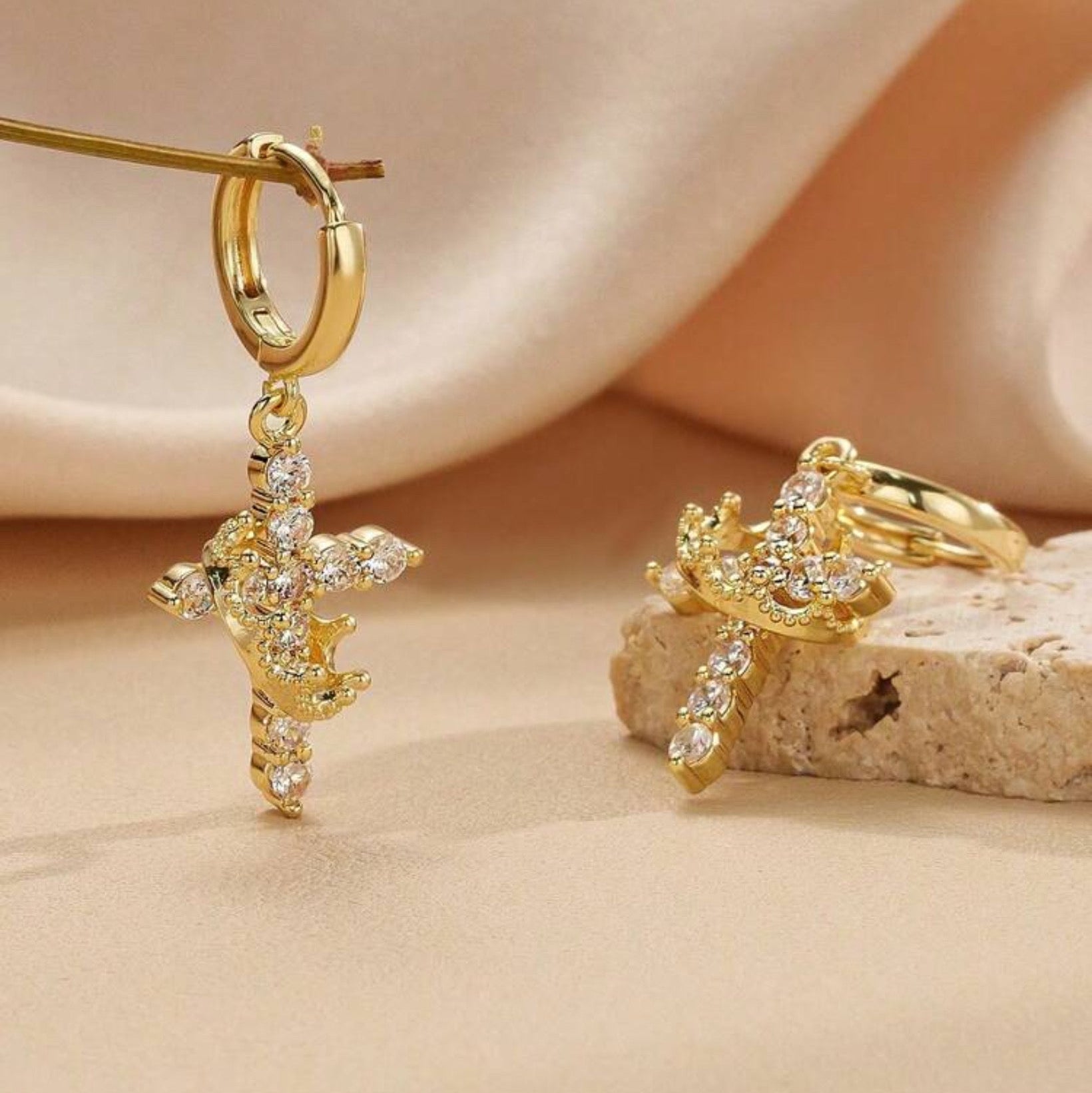 Gold Cross Crown earrings with cubic zirconia stones on a beige surface