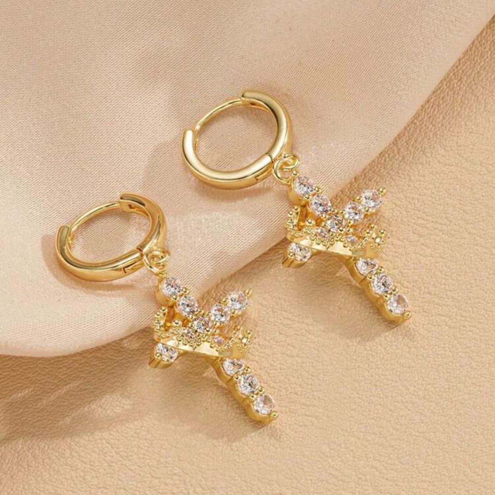 Gold Cross Crown earrings with cubic zirconia stones on a beige background