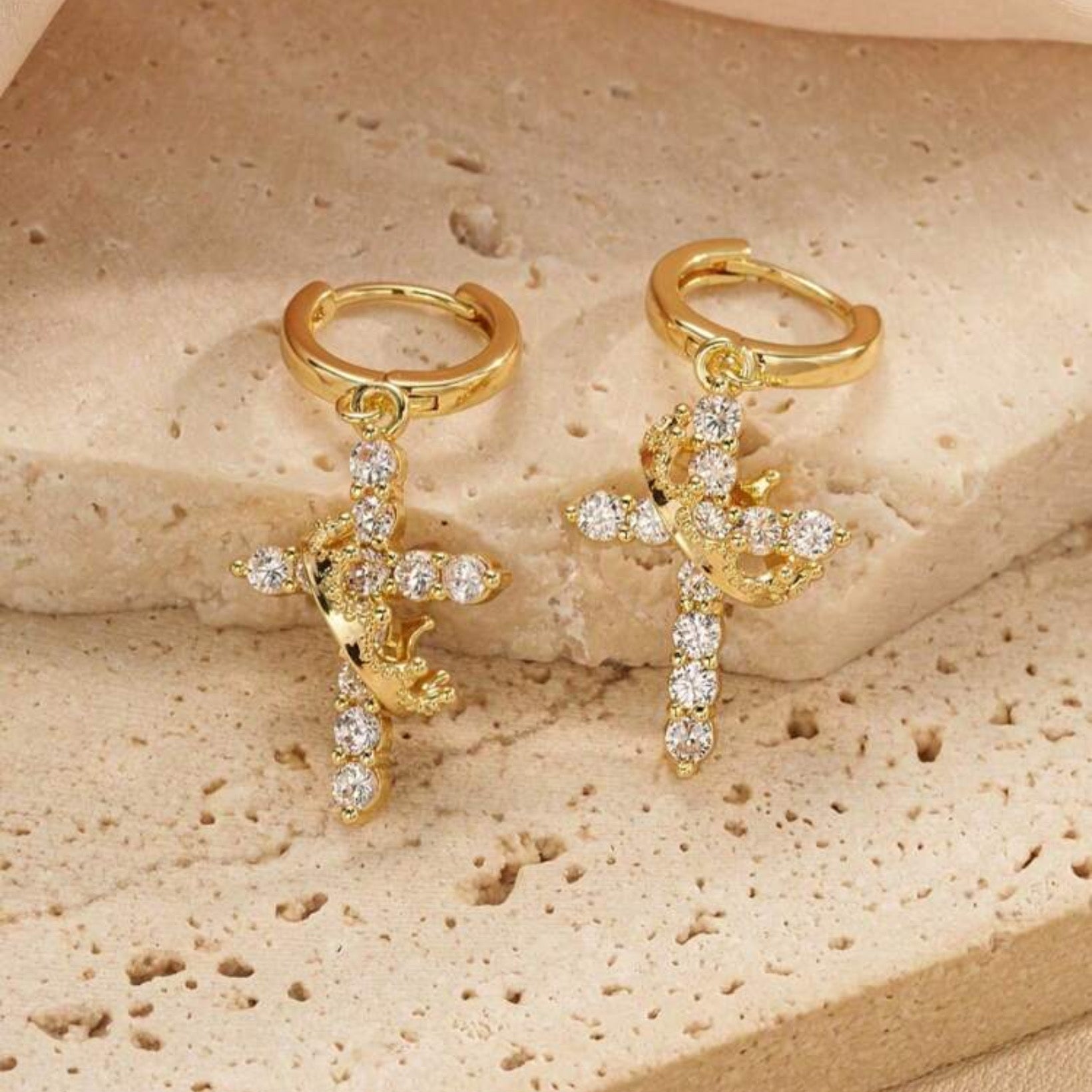 Gold Cross Crown earrings with cubic zirconia stones on a beige stone surface