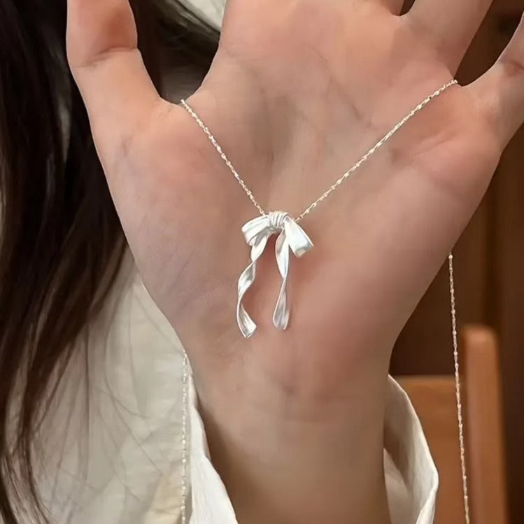 Silver Ribbon Bow Necklace with a bow pendant held by a person