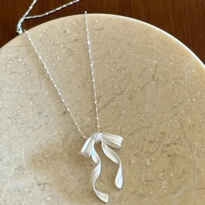 Silver Ribbon Bow Necklace with a bow pendant on a stone surface