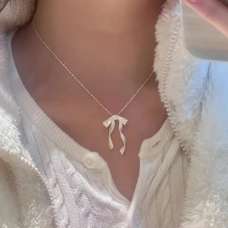 Silver Ribbon Bow Necklace with a bow pendant worn by a person in a white textured garment.