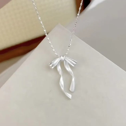 Silver Ribbon Bow Necklace with a ribbon-shaped pendant on a white surface