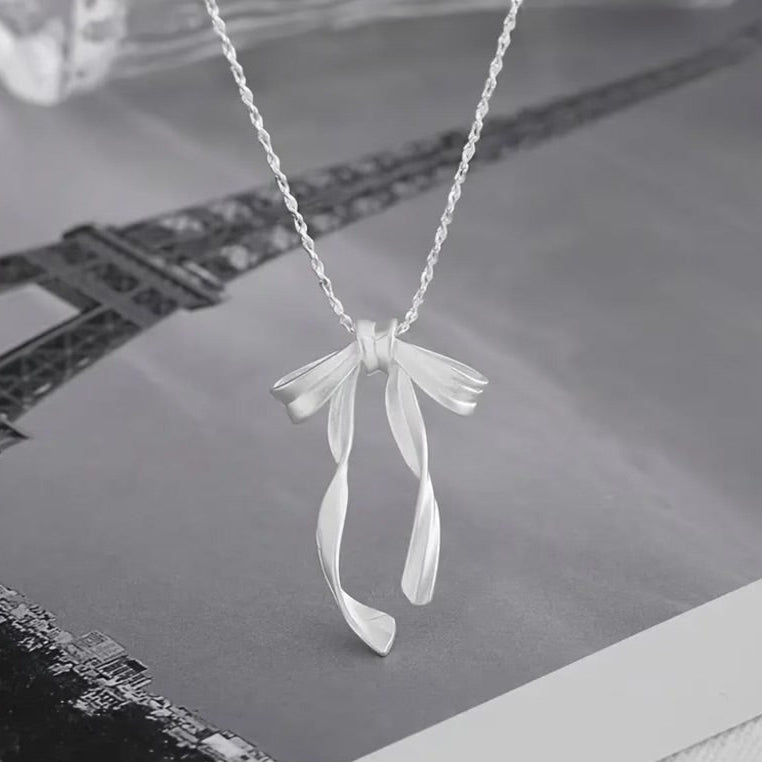 Silver Ribbon Bow Necklace on a textured surface with blurred background