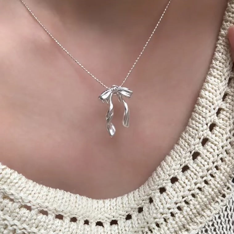 Silver Ribbon Bow Necklace with a leaf-shaped pendant worn by a person in a textured white top.
