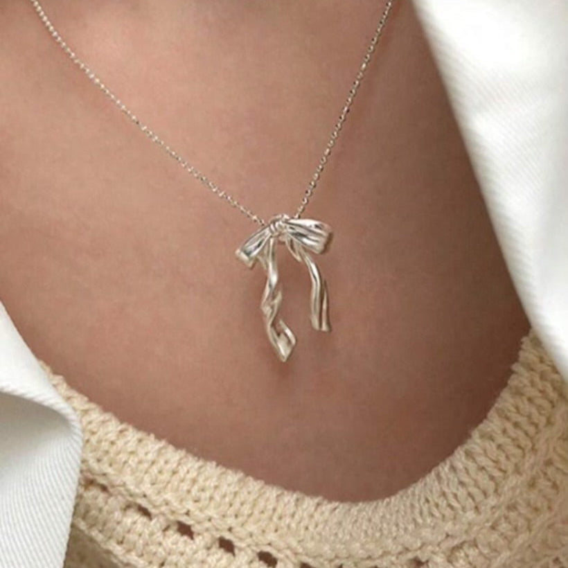 Silver Ribbon Bow Necklace with a unique pendant worn by a person against a neutral background
