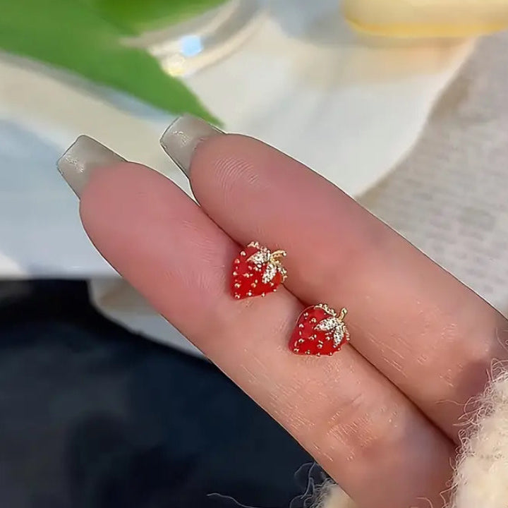 Red strawberry-shaped earrings on a finger with a blurred background