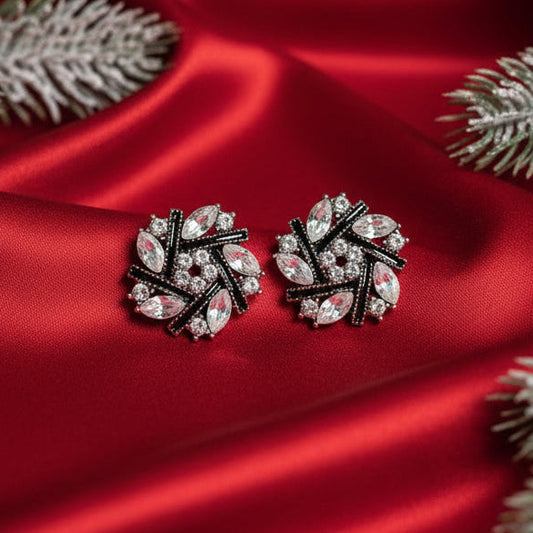 Pair of silver earrings with gemstones on a red satin surface with decorative lights and greenery.