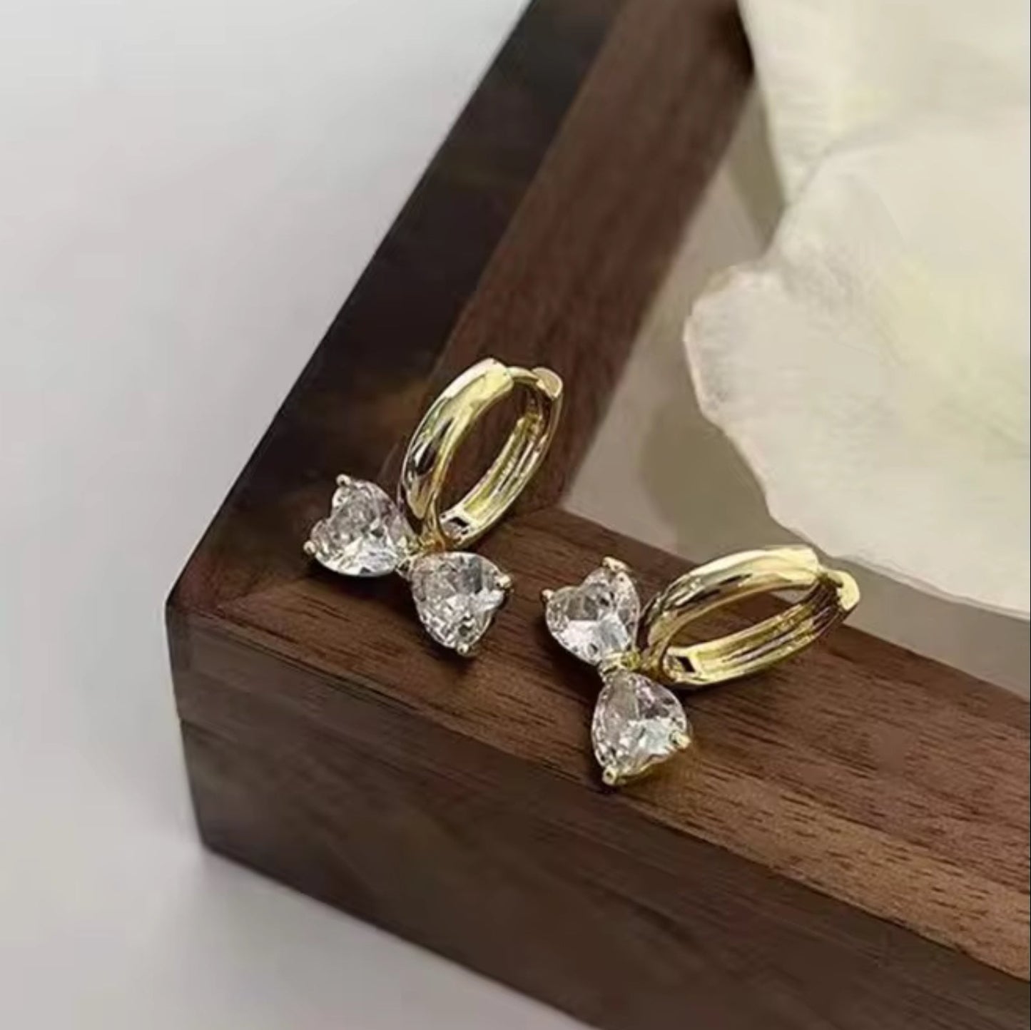 Gold Zircon Bow Hoop Earrings with clear gemstones on a wooden surface