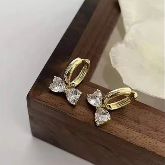 Gold Zircon Bow Hoop Earrings with clear gemstones on a wooden surface