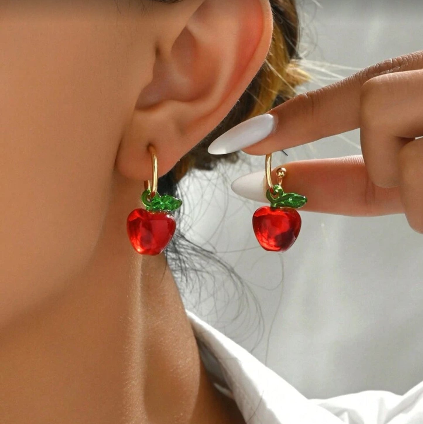 Red Apple Hoop Earrings being worn and held by a hand against a neutral background