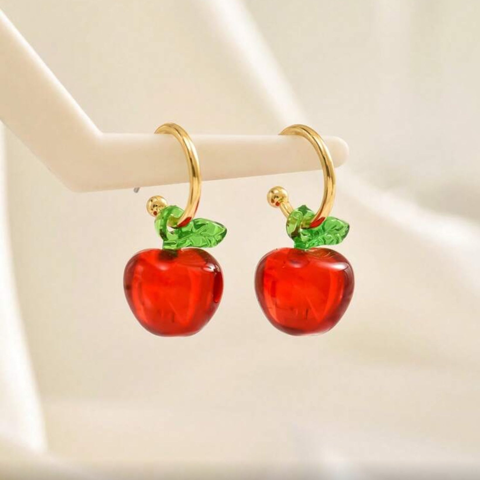 Red Apple Hoop Earrings with gold hooks on a beige background