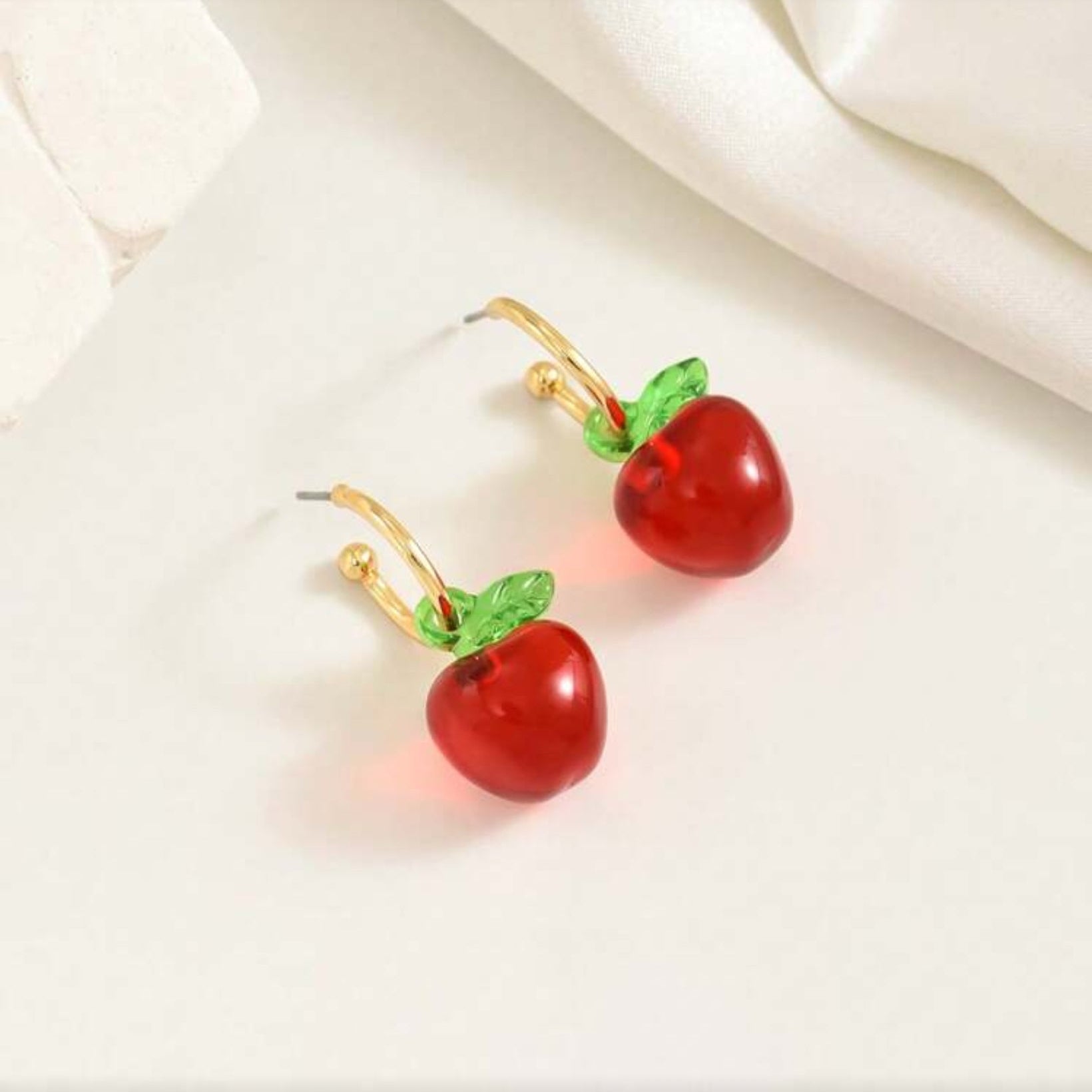 Red Apple Hoop Earrings with gold and green accents on a white fabric background