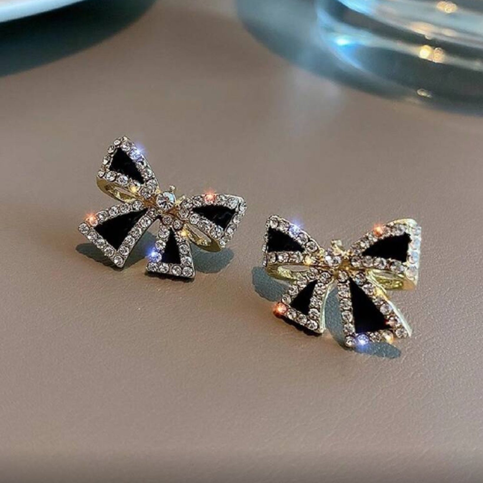 Black Bow Rhinestone Earrings with black centers and gold accents on a reflective surface.