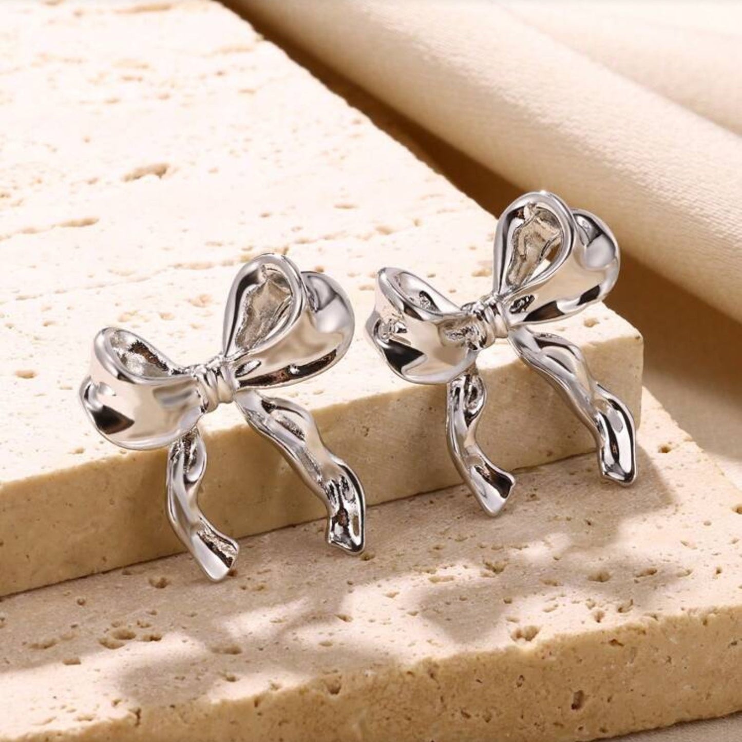 Silver Bow Ribbon Earrings on beige rock background