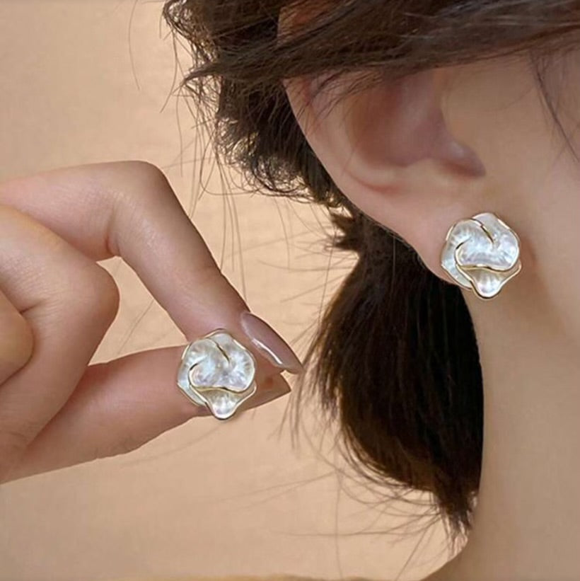 Close-up of a person wearing Golden Edge Pearl Earrings with pearl-like petal design and gold trim with a blurred background