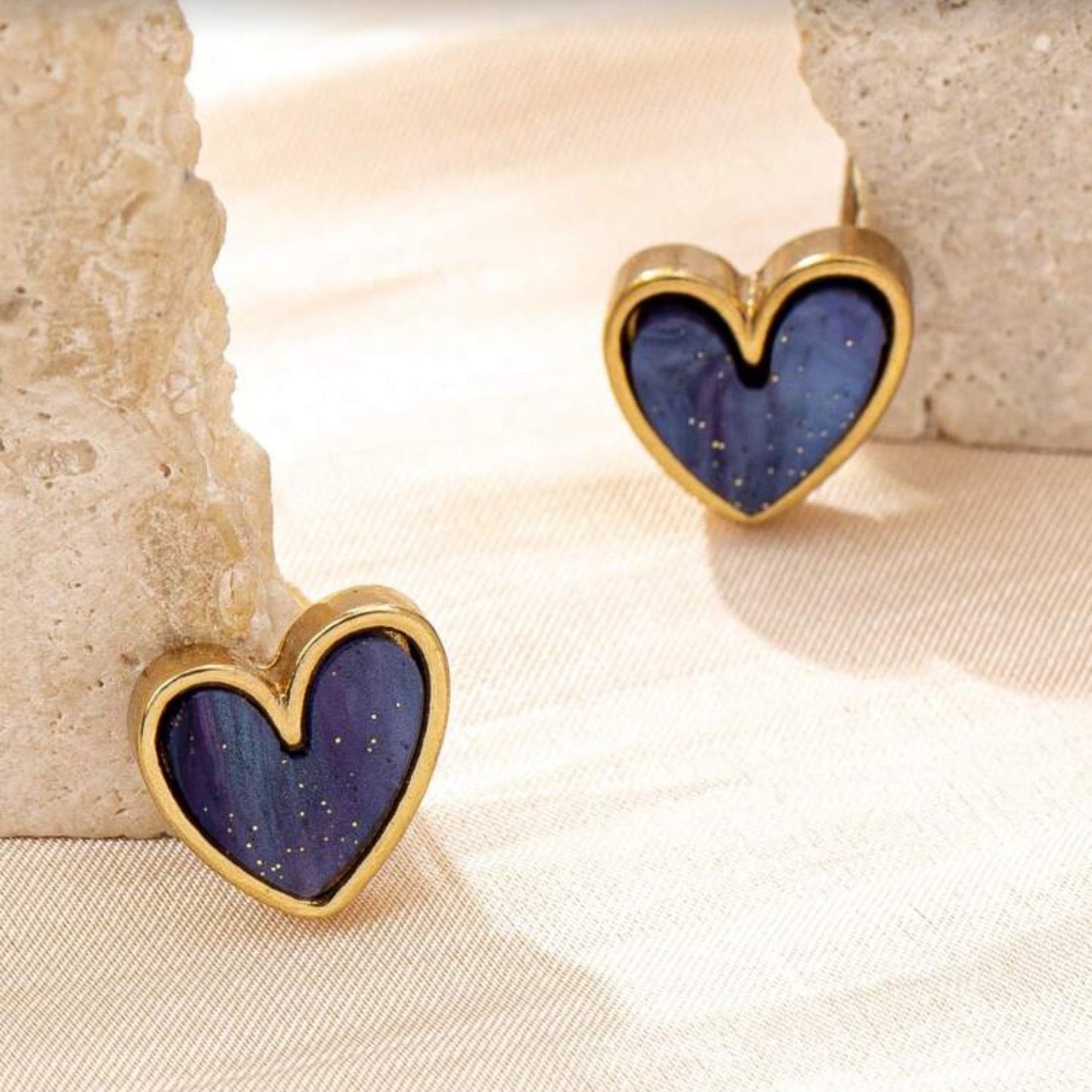 Blue Gold Dust Heart Earrings with purple centers and gold frames on a beige surface.