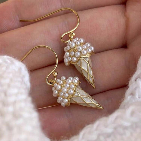 Gold earrings with pearl-like beads held in a hand against a soft background