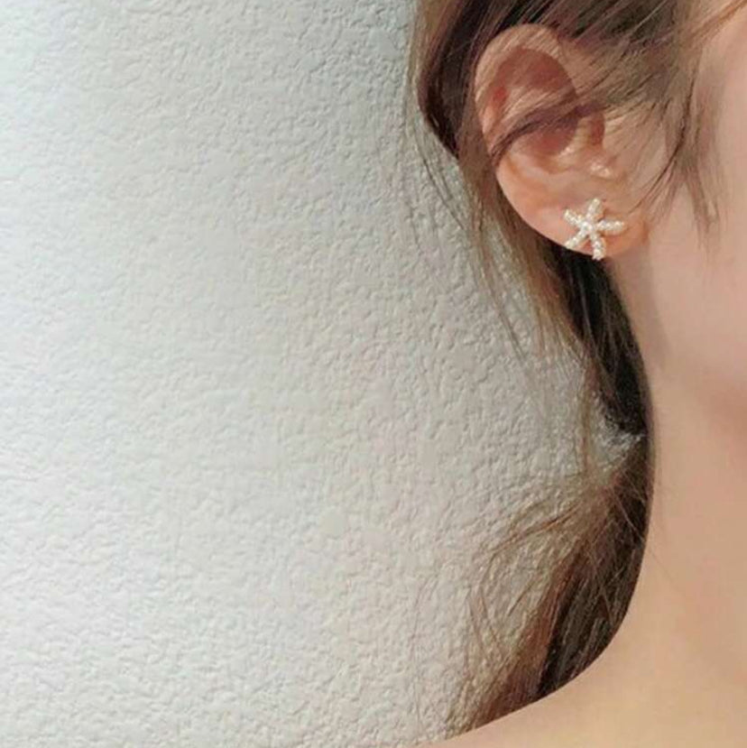 Close-up of an ear wearing a starfish pearl earring with a neutral background