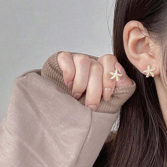 Person wearing pearl starfish-shaped earrings with a neutral background