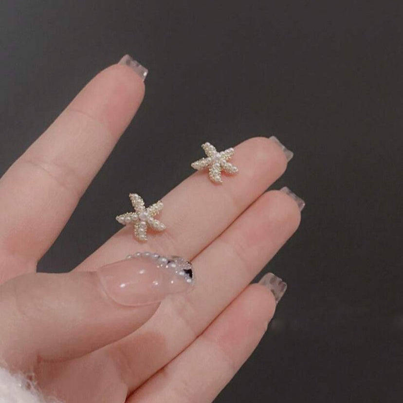 Starfish pearl earrings held by a hand against a dark background