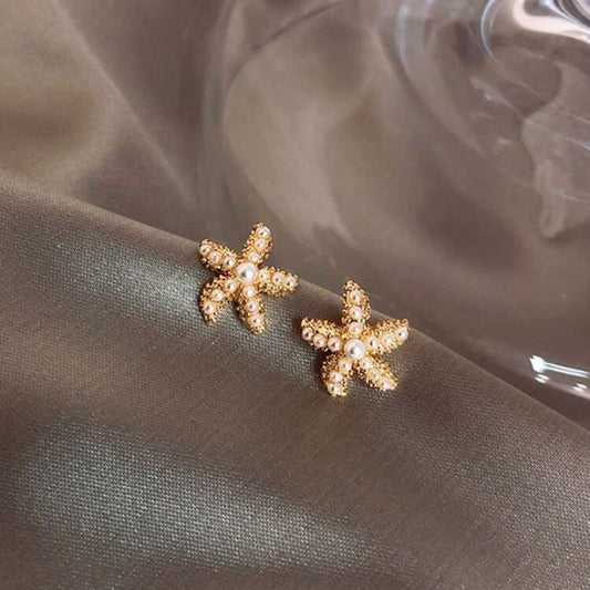 Gold starfish-shaped earrings on a textured fabric background