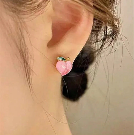 Close-up of an ear wearing a pink and green earring against a neutral background