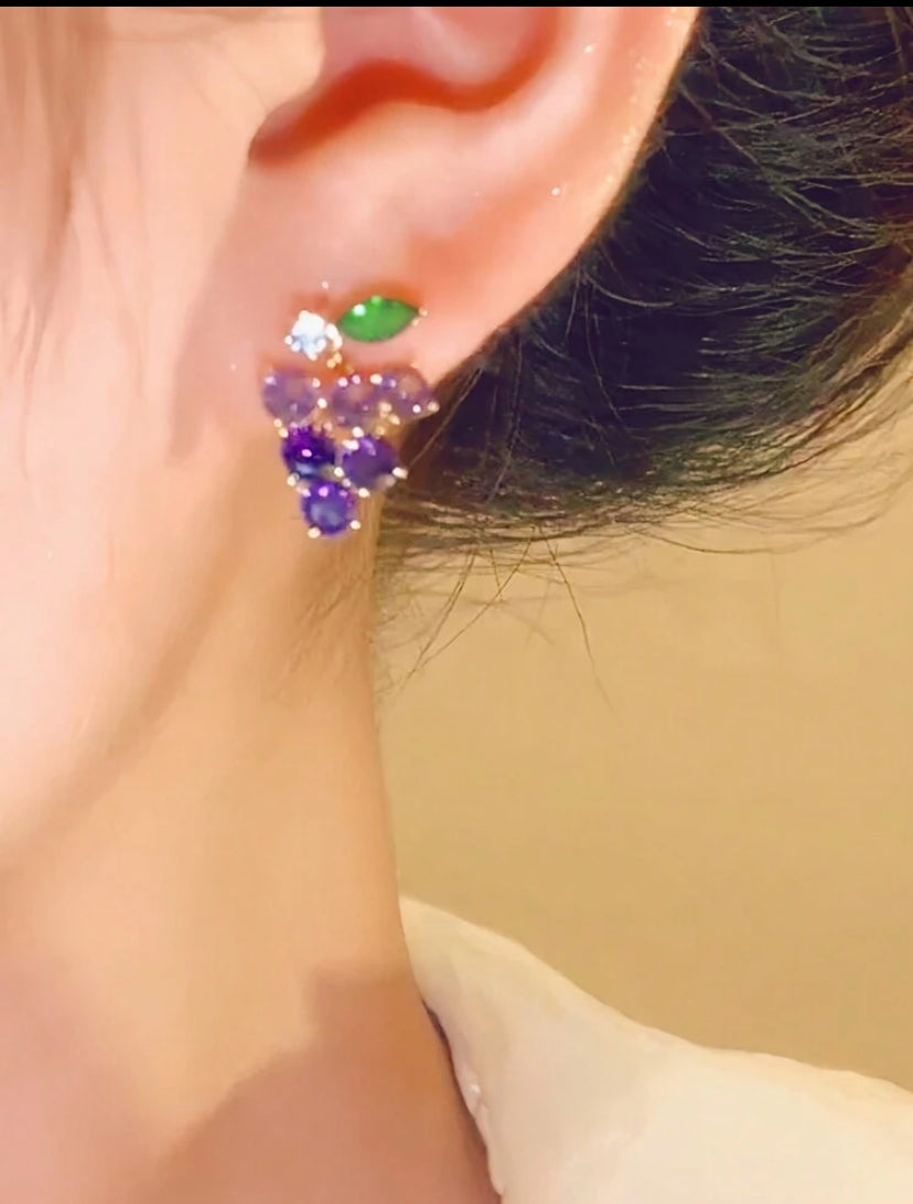 Close-up of an ear wearing a colorful grape earring with a green gemstone.