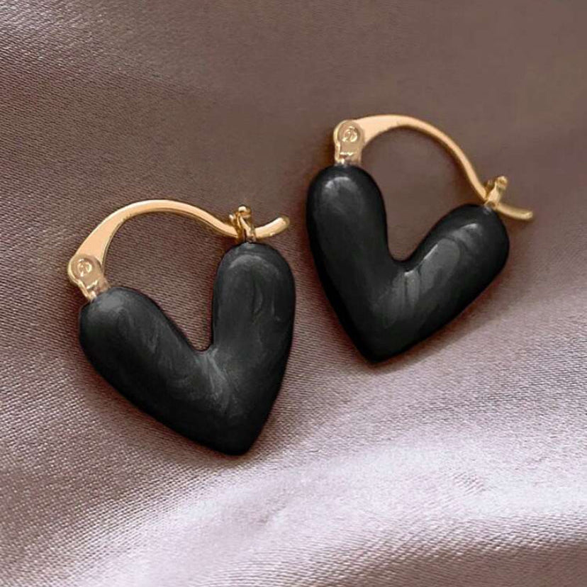 Black heart-shaped earrings with gold accents on a textured surface