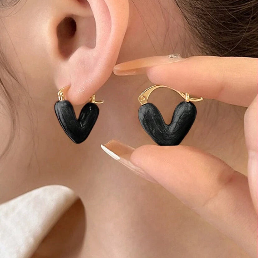 Black heart-shaped earrings being worn and held up to an ear.