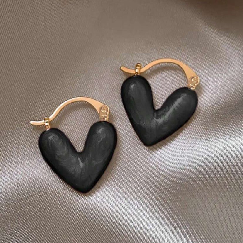 Black heart-shaped earrings with gold hoops on a beige fabric background