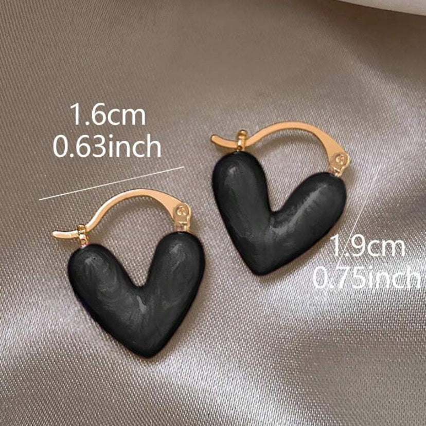 Black heart-shaped earrings with gold hooks on a beige fabric background, showing measurements.