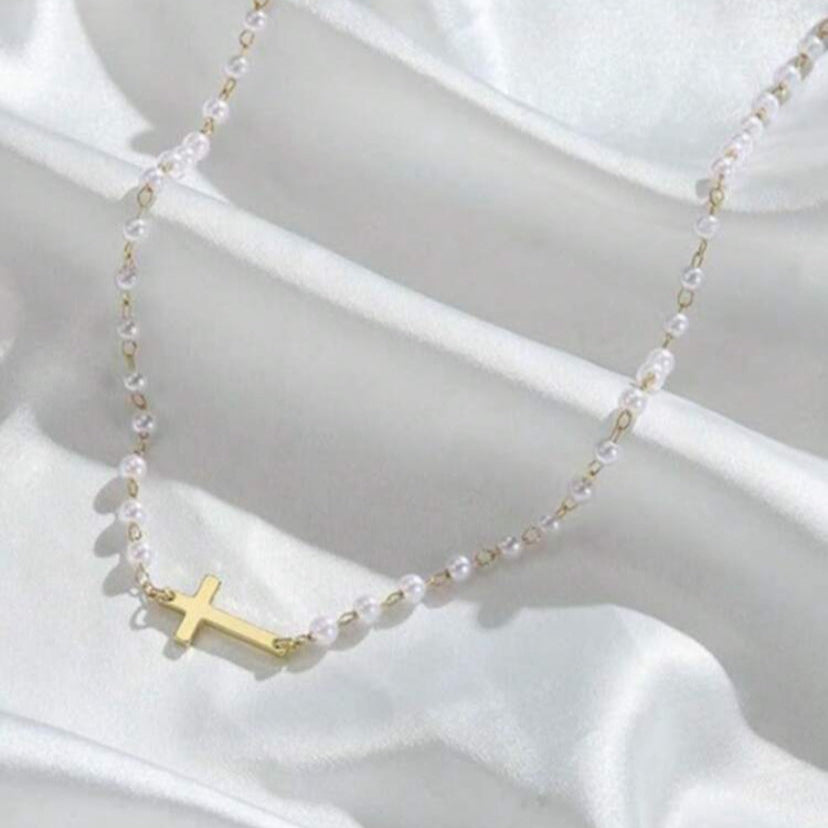 Gold Cross Pearl Necklace on a white fabric background