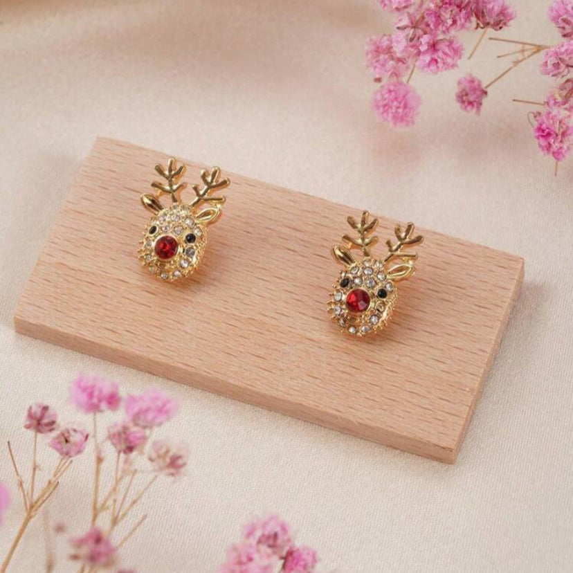 Rudolph Red Nose Reindeer Earrings on a wooden stand, surrounded by pink flowers.