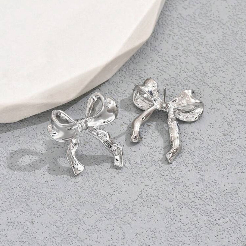 Silver Bow Ribbon Earrings on a gray surface