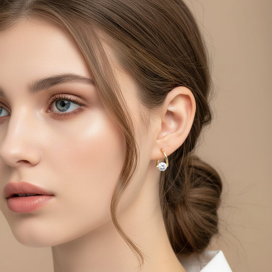 Close-up of an ear wearing a Gold Zircon Drop Hoop Earring with a clear gemstone against a neutral background.