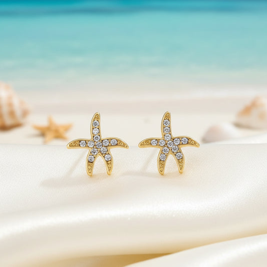 Pavé Starfish Earrings on a beach with shells