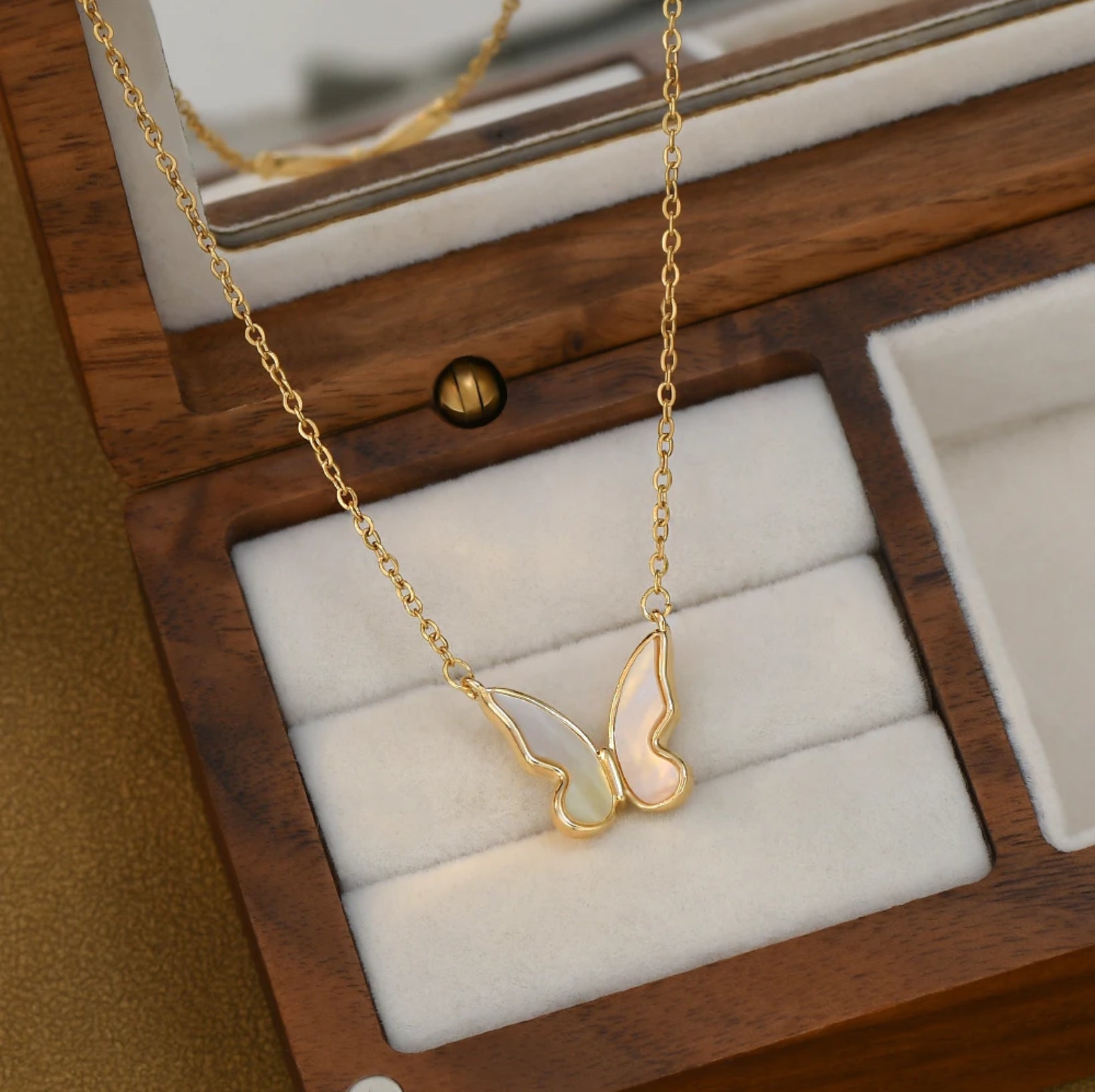 Close-up of the Shell Butterfly Necklace showing delicate mother of pearl inlay in a gold butterfly pendant on an adjustable chain, shown inside a jewelry box.